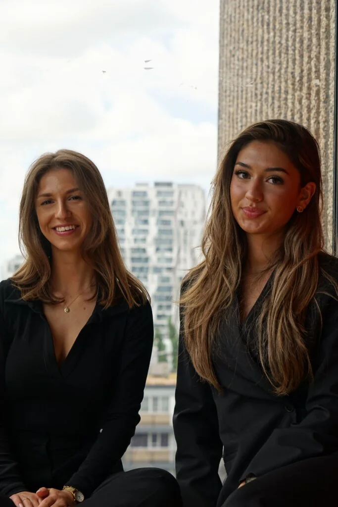 Twee lachende consultants bij het raam, met de stad op de achtergrond