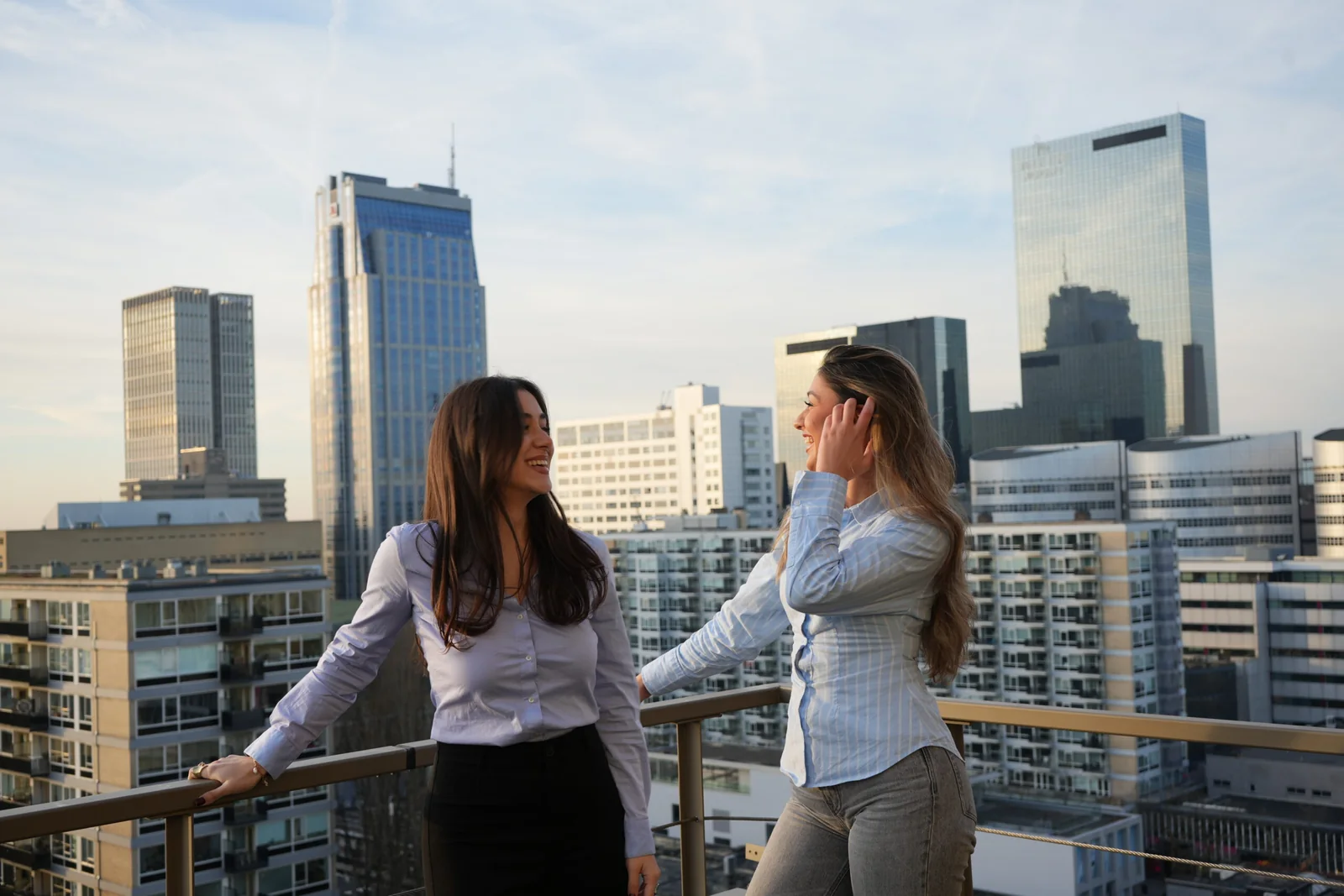 Twee collega's van 1UP Talent lachend op het dakterras met uitzicht over Rotterdam